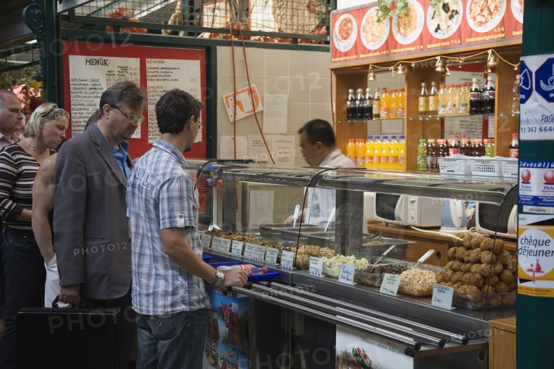 Budapest, Pest County, Hungary. Queue of customers at stall selling snacks salads and other dishes at Nagy Vasarcsarnok the Central Market. Hungary Hungarian Europe European East Eastern Buda Pest Budapest City Market markets Central Nagy Vasarcsarnok Food Snacks Fast Drinks Soft Soda Pop Customers Queue Queuing Line Destination Destinations Eastern Europe