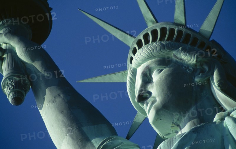 New York City, New York State, USA. The Statue of Liberty. Detail of head and arm holding torch against a blue sky. American Color Destination Destinations North America Northern Sightseeing Tourists United States of America Colour Holidaymakers Tourism