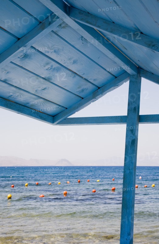 Kos, Dodecanese, Greece. View over red and yellow floats in water part framed by roof of blue painted wooden structure in foreground. Greece Greek Europe European Vacation Holiday Holidays Travel Destination Tourism Ellas Hellenic Docecanese Kos Beach Sea Blue Wooden Wood Shelter Buoys Color Destination Destinations Ellada Sand Sandy Beaches Tourism Seaside Shore Tourist Tourists Vacation Southern Europe