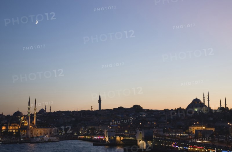 Istanbul, Turkey. Sultanahmet. The Golden Horn. The New Mosque or Yeni Camii at left the Galata Bridge and Suleymaniye Mosque at right. Buildings illuminated at dusk and crescent moon in purple blue sky above. Turkey Turkish Istanbul Constantinople Stamboul Stambul City Europe European Asia Asian East West Urban Skyline Destination Travel Tourism Sultanahmet Golden Horn New Mosque Yeni Camii Galata Bridge Suleymaniye Dusk Sunset Night Illuminated Skyline Minarets Water Crescent Moon Citiscape Building Buildings Urban Architecture Destination Destinations Middle East Nightfall Twilight Evenfall Crespuscle Crespuscule Gloam Gloaming Nite Religion Religious South Eastern Europe Sundown Atmospheric Turkiye Western Asia