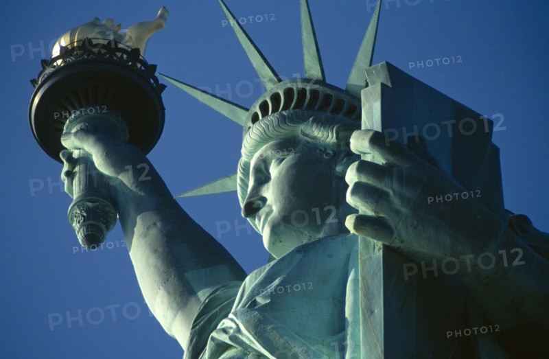 New York City, New York State, USA. The Statue of Liberty. Detail of head and arm holding torch against a blue sky. American Color Destination Destinations North America Northern Sightseeing Tourists United States of America Colour Holidaymakers Tourism