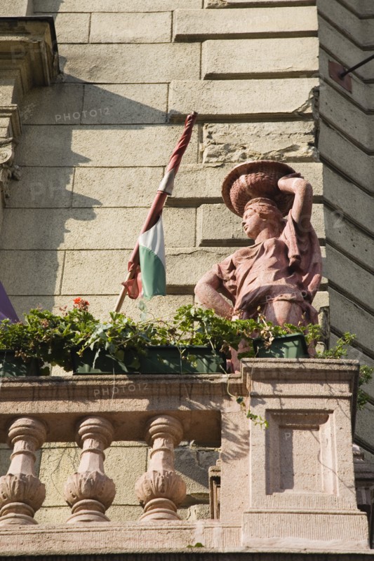 Budapest, Pest County, Hungary. Art Nouveau exterior facade with rolled Hungarian flag flower pots and statue on stone balcony. Hungary Hungarian Europe European East Eastern Buda Pest Budapest City Architecture Art Nouveau Facade Detail Stone Balcony Statue Flowers Pots Destination Destinations Eastern Europe