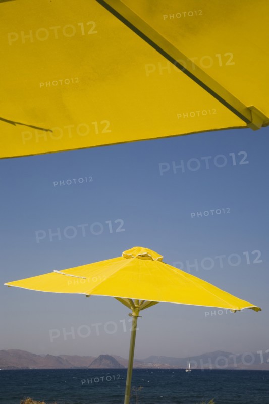 Kos, Dodecanese Islands, Greece. Bright yellow parasols on beach outside Kos Town view towards distant coastline beyond. Greece Greek Europe European Vacation Holiday Holidays Travel Destination Tourism Ellas Hellenic Docecanese Kos Sea Sea Umbrella Umbrellas Parasol Parasols Yellow Blue Color Destination Destinations Ellada Sand Sandy Beaches Tourism Seaside Shore Tourist Tourists Vacation Southern Europe Water