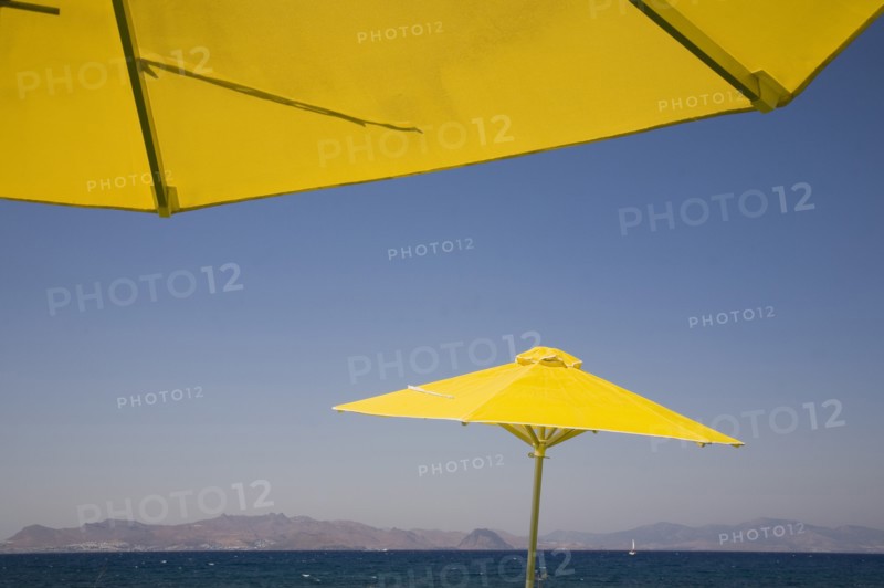 Kos, Dodecanese Islands, Greece. Bright yellow parasols on beach outside Kos Town with view towards distant coastline beyond. Greek Europe European Vacation Holiday Holidays Travel Destination Tourism Ellas Hellenic Docecanese Kos Beach Sea Umbrella Umbrellas Parasol Parasols Yellow Blue Color Destination Destinations Ellada Sand Sandy Beaches Tourism Seaside Shore Tourist Tourists Vacation Southern Europe Water