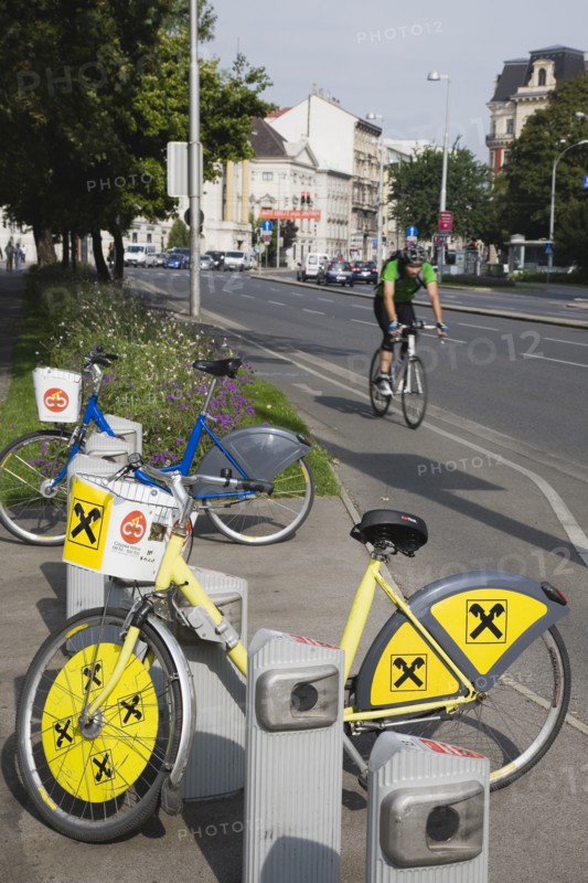 Vienna, Austria. Neubau District. Bicycles for use in city centre with approaching cyclist on road behind. Austria Austrian Republic Vienna Viennese Wien Europe European City Capital Neubau District Urban Transport Bicycle Bike Bicycles Bikes Cycle Cyclist Pay Hire Rent Center Destination Destinations One individual Solo Lone Solitary Osterreich Viena Western Europe