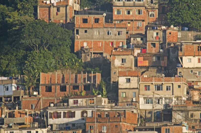 Rio de Janeiro, Brazil. Favela or slum on hillside above Copacabana neighbourhood red brick houses greenery and TV dish antenna. Brazil Brasil Brazilian Brasilian South America Latin Latino American City Urban Architecture Houses Housing Homes Copacabana Neighborhood Neighbourhood Favela Favelas Slum Slums Church Rio de Janeiro Aerial Destination Destinations Latin America Shanty South America Southern