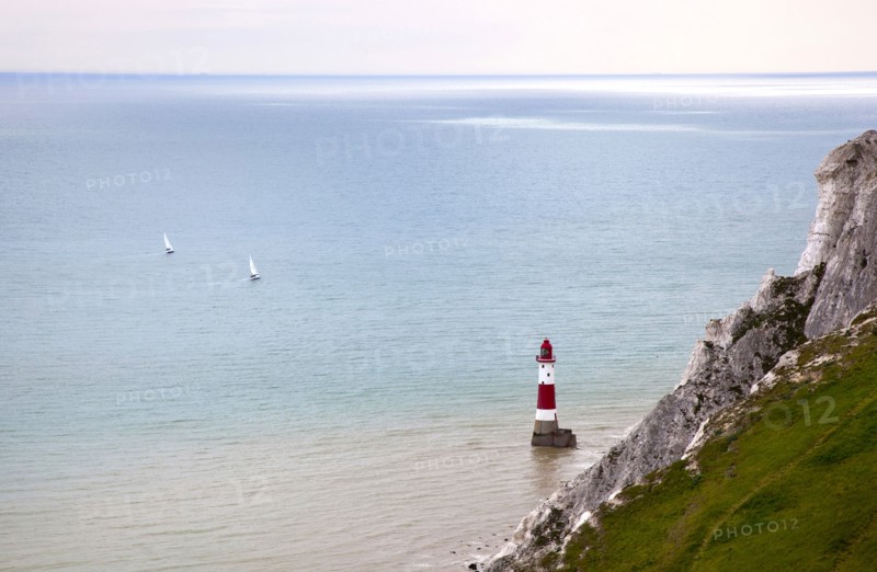 Eastbourne, East Sussex, England. Beachy Head view of the lighthouse at the base of the chalk cliffs. England English UK United Kingdom GB Great Britain Birtish East Sussex County Eastbourne Beachy Head Sea Coast Chalk Cliff Cliffs White Lighthouse Light House Boat Ship Transport Warning