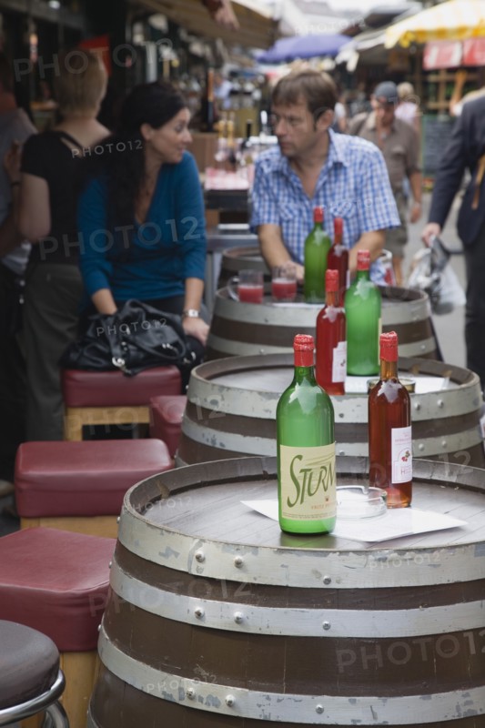 Vienna, Austria. Young couple having glass of Federweisser wine in the fermentation stage known as Sturm in Austria seated at outside table made from a barrel. Due to the carbonic acid Federweisser tastes quite refreshing not unlike a grape lemonade or a sweet sparkling wine. Austria Austrian Republic Vienna Viennese Wien Europe European City Capital Market Drink Drinks Alcohol Wine Federweisser Fermentation Sturm Barrel Barrels Couple Destination Destinations Immature Osterreich Viena Vino Vin Alcohol Grape Winery Drink Western Europe