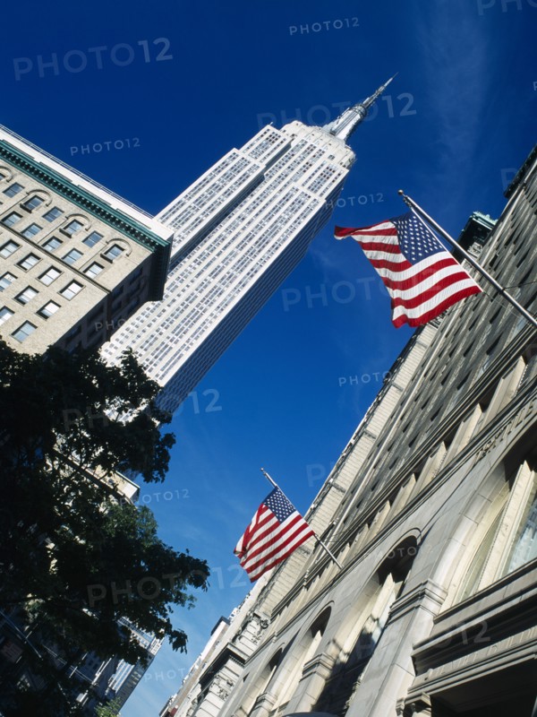 Manhattan, New York, USA. Angled view looking up at the Empire State Building and building facades flying American flags on 5th Avenue North America United States of America