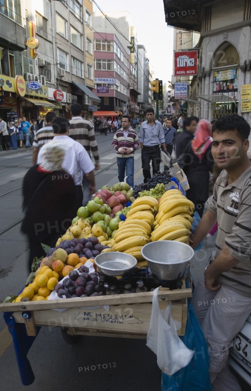 Istanbul, Turkey. Sultanahmet. Fresh fruit stall beside tramway on busy street. Turkey Turkish Istanbul Constantinople Stamboul Stambul City Europe European Asia Asian East West Urban Destination Travel Tourism Sultanahmet Street Market Stall Vendor Fruit Busy People Crowded Crowd Destination Destinations Middle East South Eastern Europe Turkiye Western Asia