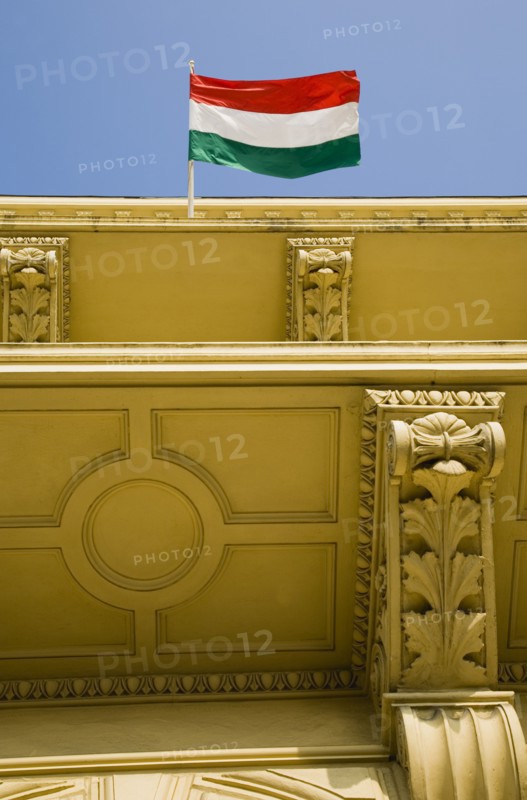 Budapest, Pest County, Hungary. Hungarian flag flying from partly seen rooftop of renovated building facade on Pest bank of the River Danube. Hungary Hungarian Europe European East Eastern Buda Pest Budapest City Architecture Flag Tricolor Tricolour Green White Red Detail Blue Sky Destination Destinations Eastern Europe