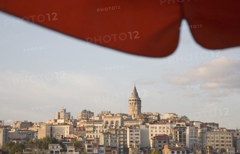 Istanbul, Turkey. Sultanahmet. View to Galata Tower from shade of red canopy alongside Galata bridge. Turkey Turkish Istanbul Constantinople Stamboul Stambul City Europe European Asia Asian East West Urban Destination Travel Tourism Sultanahmet Bosphorous Galata Tower Cityscape Rooftops Skyline Red Canopy Blue Citiscape Building Buildings Urban Architecture Clouds Cloud Sky Color Destination Destinations Middle East South Eastern Europe Turkiye Western Asia