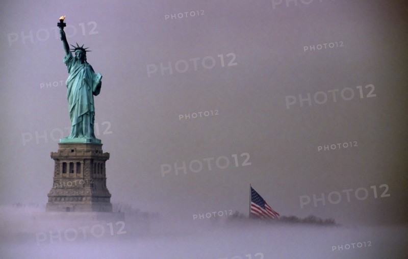 Liberty Island, New York, USA. Statue of Liberty and Stars and Stripes Flag on misty morning. USA United State States America American New York City Liberty Island Statue Copper Metal Figure Female Green Torch Mist Fog Moody Flag Stars Stripes History Historic North America Northern Surly United States of America