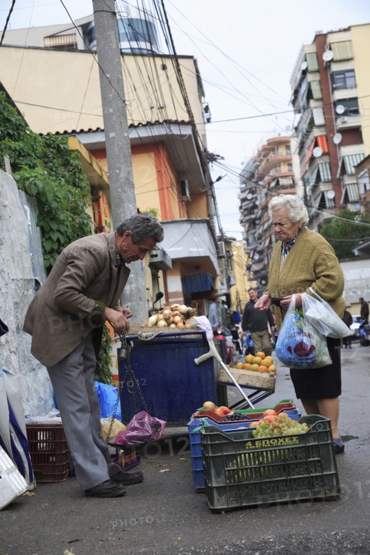 Albania, Tirane, Tirana, A street vendor using hand held set of scales to weigh fruit for elderly woman customer carrying bags.