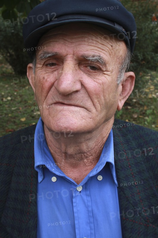 Albania, Berat, Head and shoulders portrait of an elderly man wearing cap and open-neck shirt.