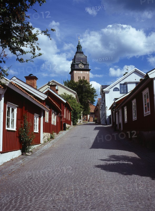 Sweden, Sodermanland, Strangnas, Cobbled street lined by wooden houses leading to Domkyrkan Cathedral  part seen exterior facade and clock tower.