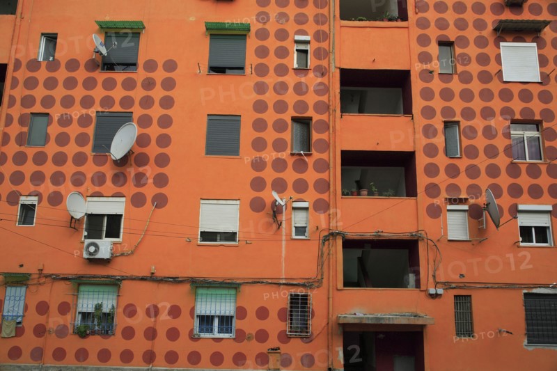 Albania, Tirane, Tirana, Part view of exterior facade of apartment block painted orange with pattern of red painted circles. Multiple windows  satelite dishes  balconies.