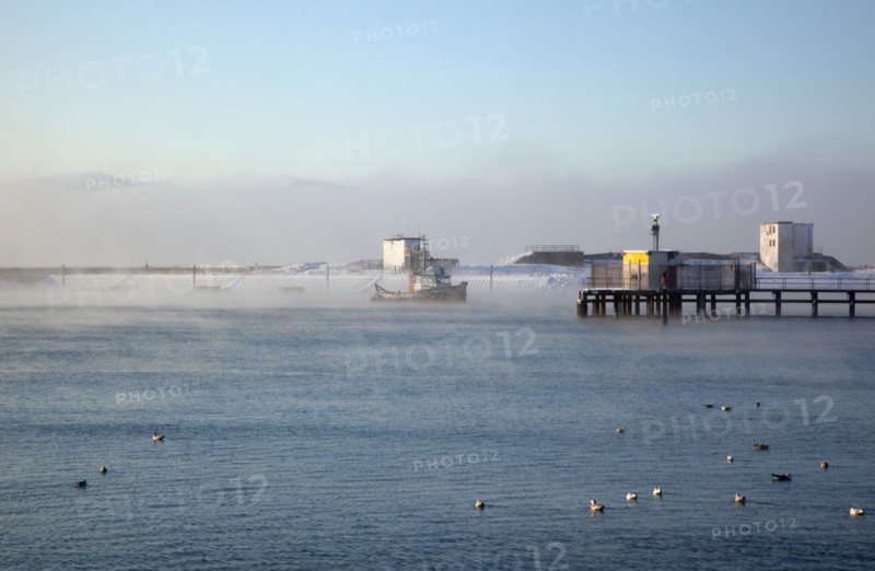 England, West Sussex, Shoreham-by-Sea , Mist rising from harbour waters on frosty morning with tug boat on the river