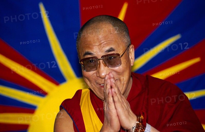 China, Tibet, Religious, The Dalai Lama smiling with hands raised in a traditional anjali greeting gesture.  Vibrant image of a yellow sun in the background.