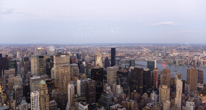 USA, New York, New York City, Manhattan  View from Empire State building over midtown skyscrapers and East River towards Queens and Long Island with Art Deco Chrysler Building illuminated at dusk.