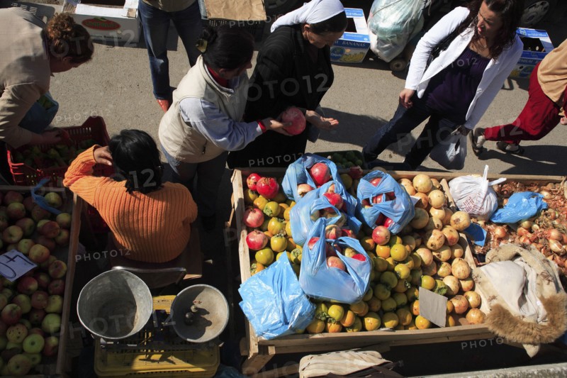 Albania, Tirane, Tirana, Looking down on stall of street vendor selling apples  pomegranates and onions sitting beside set of scales with female customers making purchases.