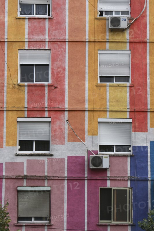 Albania, Tirane, Tirana, Detail of exterior facade of striped  multi-coloured apartment block with windows  window blinds and air conditioning units.