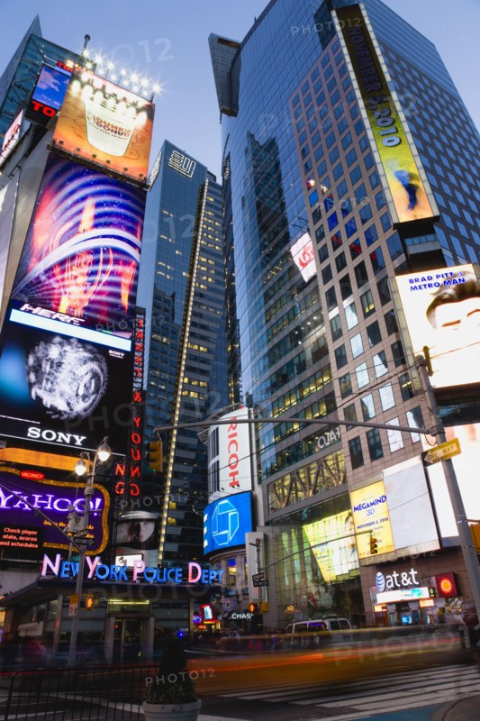 USA, New York, New York City, Manhattan  People walking at night in Times Square at the junction of 7th Avenue and Broadway by the New York Police Department station below buildings with advertising on large video screens.