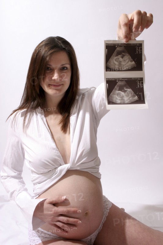 Health, Pregnancy, Scan, Young  pregnant woman holding up her ultrasound scan photograph with one hand  the other resting on her stomach.