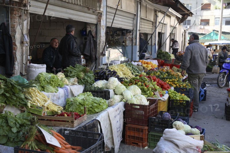 Albania, Tirane, Tirana, Customer and vendors at fruit and vegetable stalls in the Avni Rustemi market with display including carrots  lettuce  aubergines  peppers and oranges.