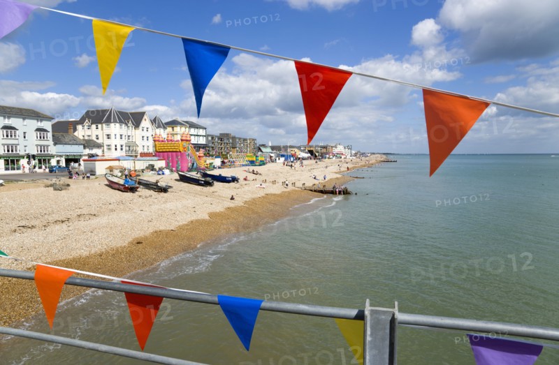 England, West Sussex, Bognor Regis, The pebble shingle beach and seafront with tourists seen through colourful flags hanging from the pier.