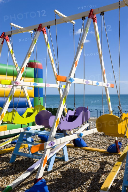 England, West Sussex, Bognor Regis, Colourful amusement swings on the pebble shingle beach by the promenade.