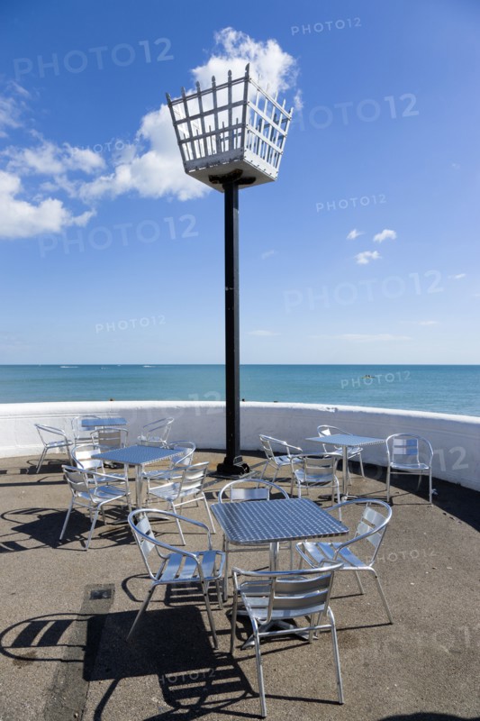 England, West Sussex, Bognor Regis, Millennium Beacon on the seafront beside the beach with empty metal tables and chairs below it on the promenade.