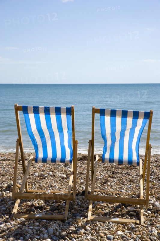 England, West Sussex, Bognor Regis, Two blue and white deck chair on the shingle pebble beach looking out to sea.