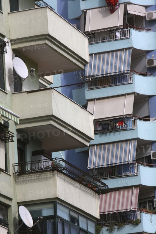 Albania, Tirane, Tirana, Detail of balconies  striped awnings and satellite dishes on blue painted exterior facade of apartment block.