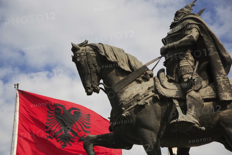 Albania, Tirane, Tirana, Skanderbeg Square. Part view of equestrian statue of national hero George Castriot Skanderbeg also known as The Dragon of Albania beside red flag with double headed eagle emblem.