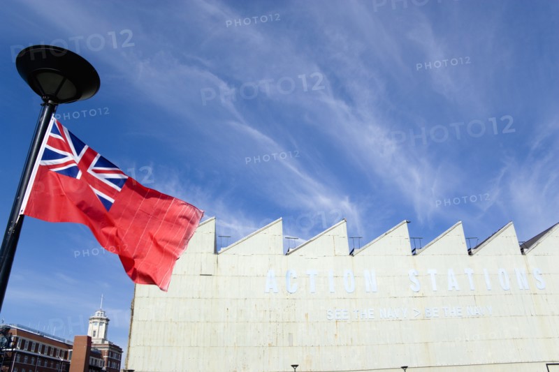 Historic Naval Dockyard Red Ensign merchant marine flag flying from flagpole with Action Stations exhibition sign on building. Photo: Paul Seheult