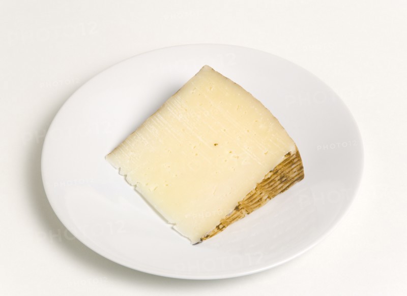 Slice of Spanish Manchego cheese made from pasteurised Manchega sheeps milk from the La Mancha region of Spain on a plate against a white background. Photo: Paul Seheult