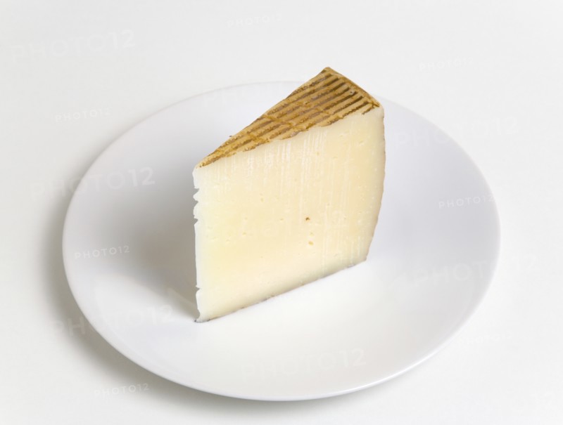 Slice of Spanish Manchego cheese made from pasteurised Manchega sheeps milk from the La Mancha region of Spain on a plate against a white background. Photo: Paul Seheult
