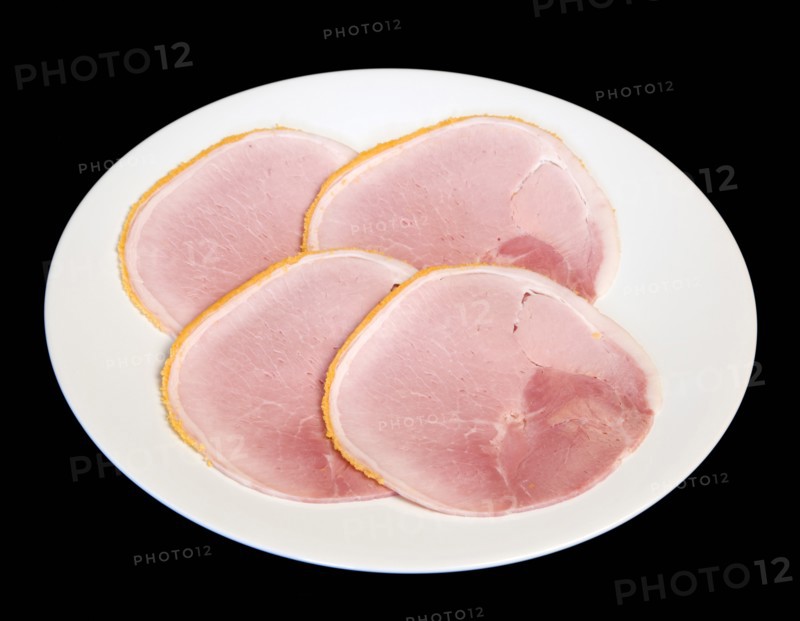 Slices of cured ham on a round white plate on a black background. Photo : Paul Seheult