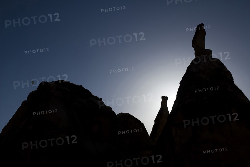 Distant hot air balloon in flight over silhouetted landscape of eroded rock forms. Photo: Hugh Rooney