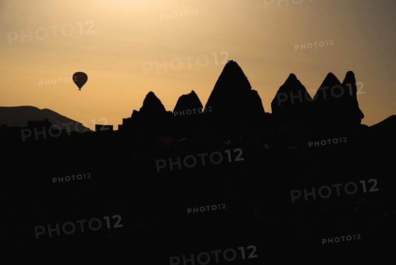 Distant hot air balloon in flight over silhouetted landscape of eroded rock forms. Photo : Hugh Rooney