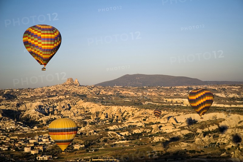 Hot air balloons in flight over landscape in early morning sunlight with Uchisar town in background.. Photo : Hugh Rooney