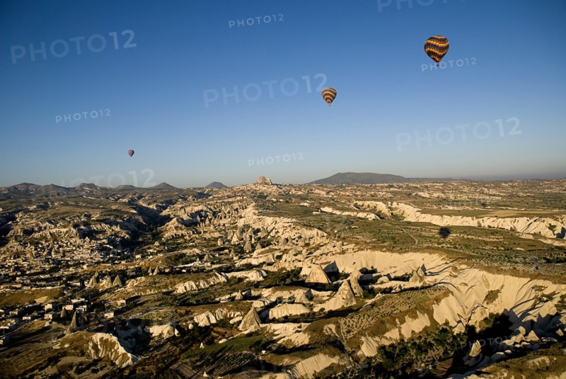 Hot air balloons in flight over landscape in early morning sunlight with Uchisar town in background and Goreme to the left.. Photo : Hugh Rooney