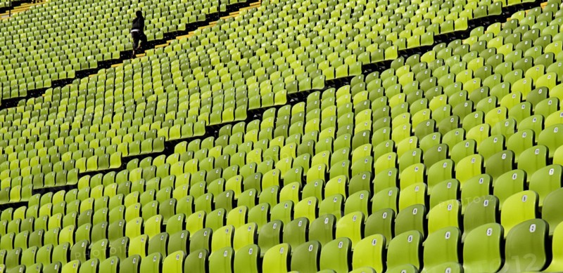 Olympic Stadium. Curved section of bright green seating in the stadium with standing figure at far end. Photo: Hugh Rooney