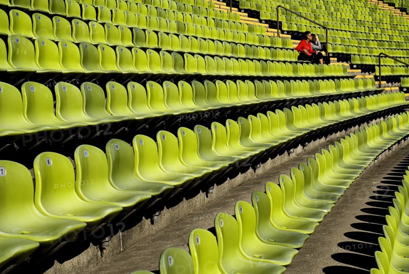 Olympic Stadium. Curved section of bright green seating in the stadium with couple seated at far end. Photo: Hugh Rooney