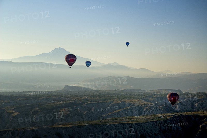 Early morning with hot air balloons in flight above tufa landscape with Mount Erciyes in the background. Photo : Hugh Rooney