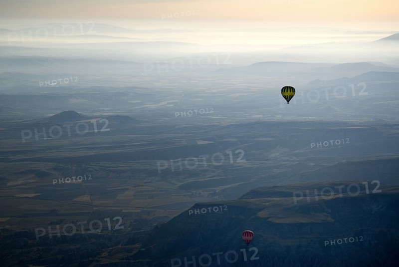 Hot air balloons in flight over landscape in misty early morning light with pale orange sky. Photo : Hugh Rooney