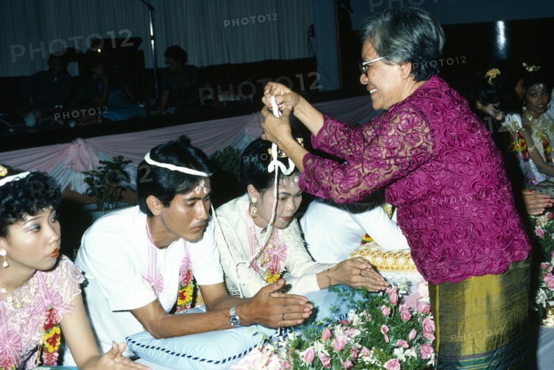 Couple being symbolically bound together with cotton at Thai Buddhist wedding ceremony. Photo : Nancy Durrell McKenna