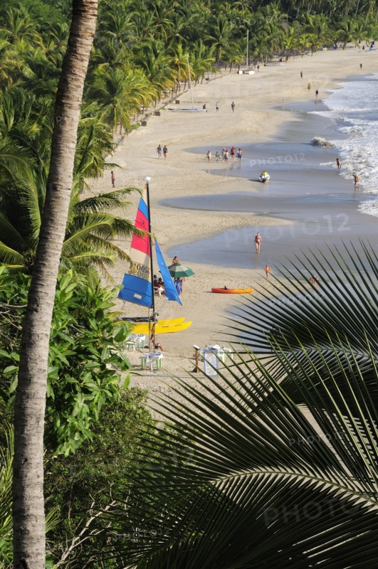 Mexico, Guerrero, Zihuatanejo, View onto Playa la Ropa with a colourful sailboat on sandy beach lined with palm trees. 
Photo : Nick Bonetti