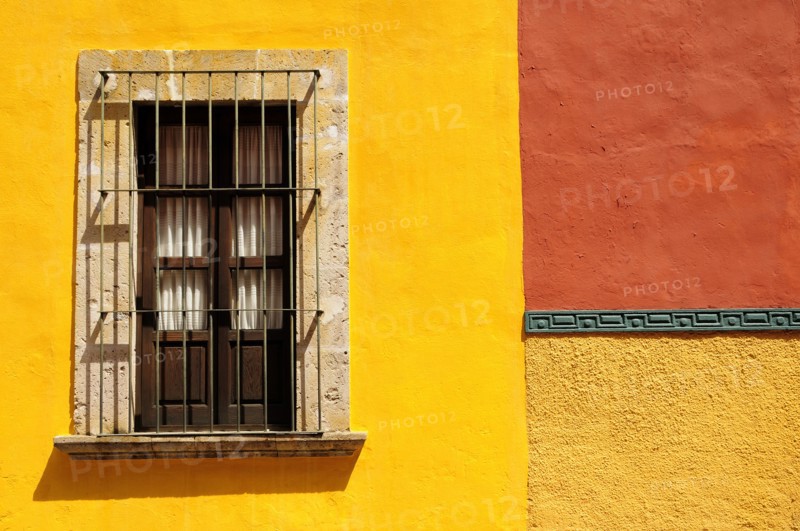 Mexico, Bajio, San Miguel de Allende, Detail of exterior wall of bright yellow and orange painted buildings with window with closed shutter and metal grill. 
Photo : Nick Bonetti